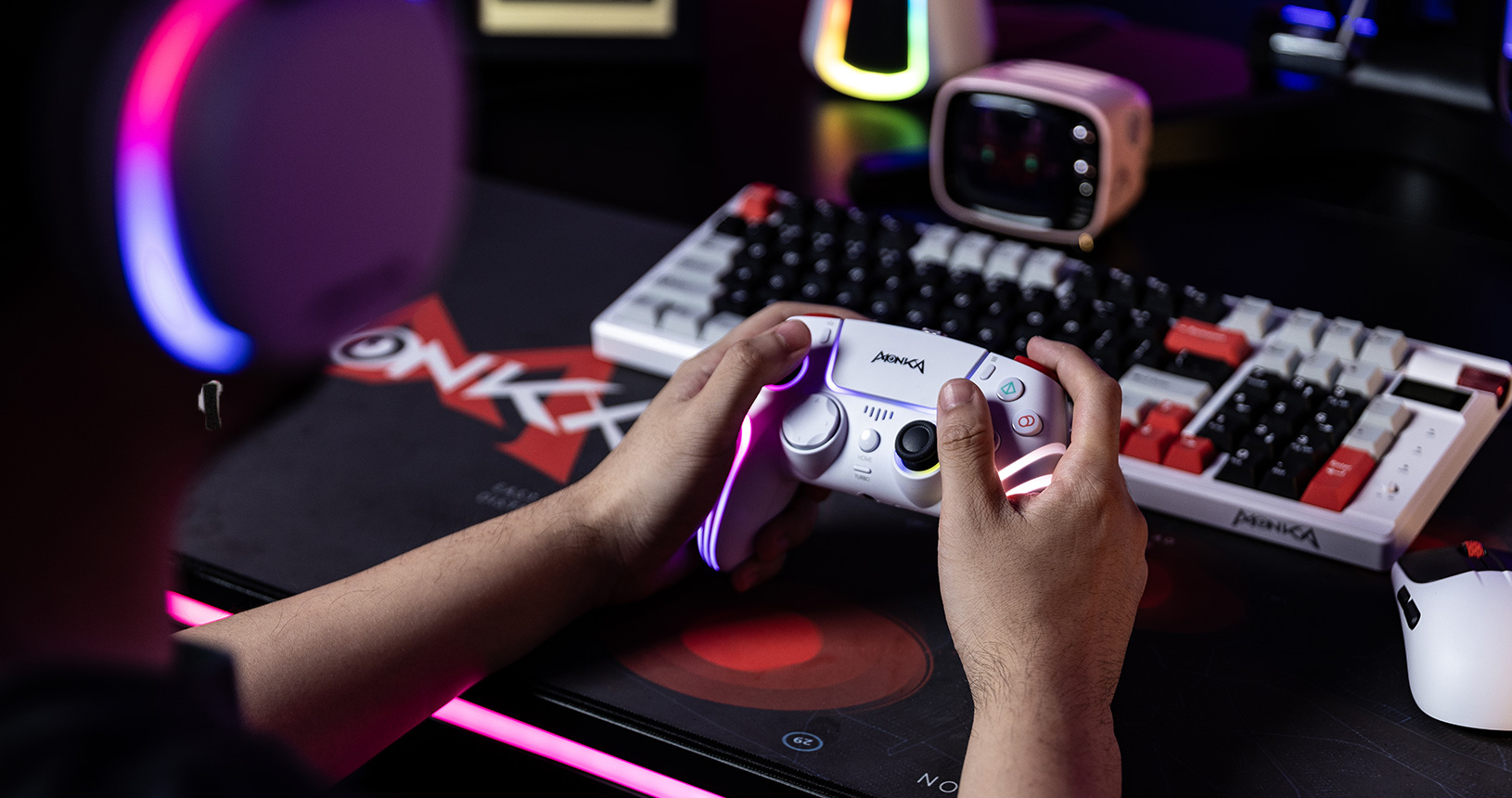 A gamer holding a modern white gaming controller with colorful LED accents, surrounded by a mechanical keyboard and gaming mouse on a stylish mouse pad, in a dimly lit gaming setup.